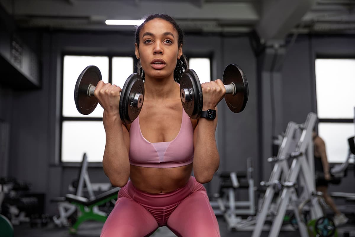 Mujer haciendo ejercicios de bíceps con mancuernas en el gimnasio, enfocada en su entrenamiento