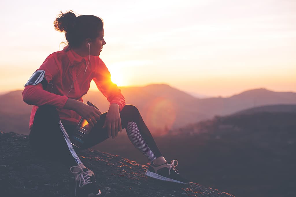 Mujer joven vestida de deporte descansando con vistas al atardecer