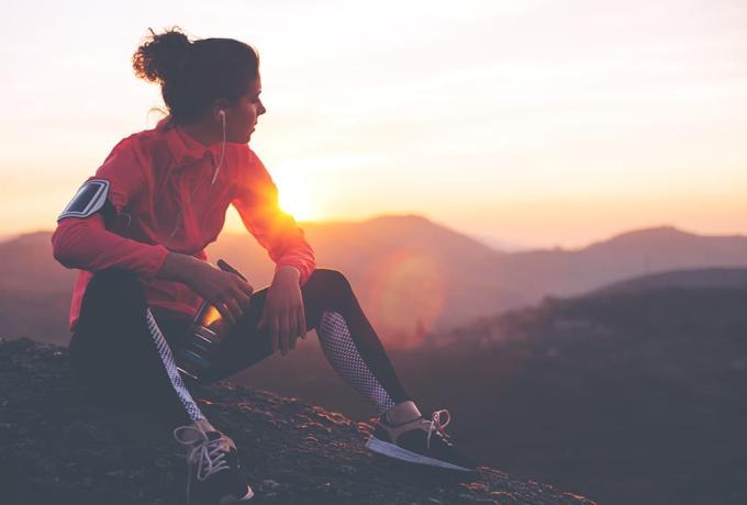 Mujer joven vestida de deporte descansando con vistas al atardecer